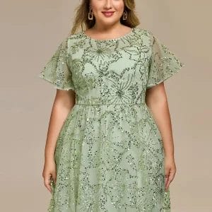 A woman wearing a light green, short-sleeve, floor-length dress with floral sequin patterns stands against a plain beige background.