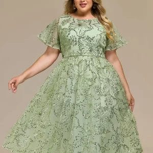 Woman wearing a light green, knee-length dress with short sheer sleeves and a sequin leaf pattern, standing against a plain background.